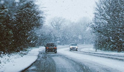 two cars driving on a snowy road intersecting a forest