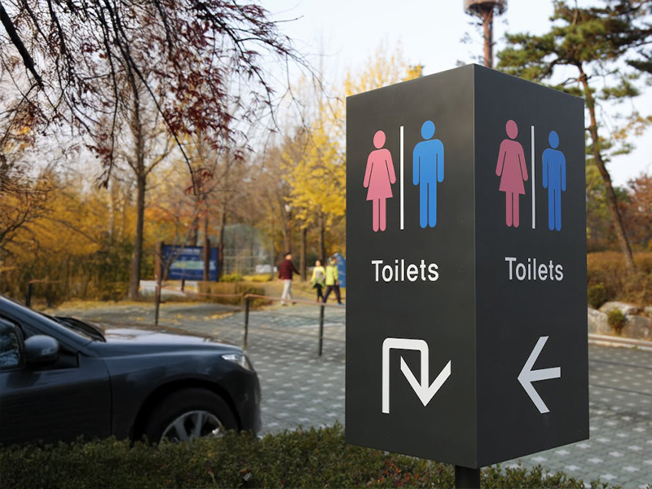 Public toilet sign in a car park with male and female symbols and directional arrows