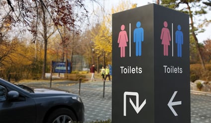 Public toilet sign in a car park with male and female symbols and directional arrows