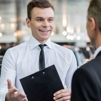 car dealer with clipboard talking to customer