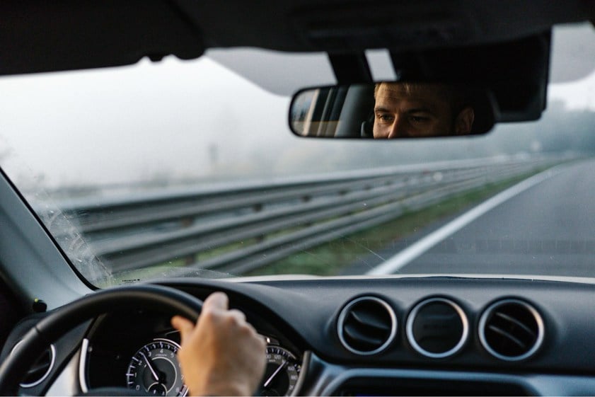 Man driving a car looking at the road ahead with reflection in the rear view mirror