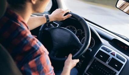 Close up of young man with hands on car steering wheel.