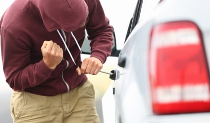 Man in a hooded top breaking into a car with a screwdriver in order to steal it.