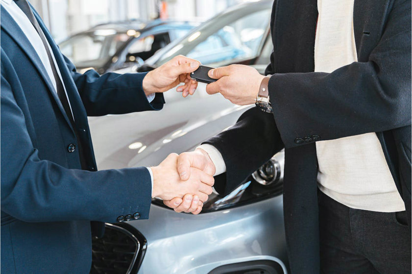 Two people shaking hands in a car showroom and exchanging keys