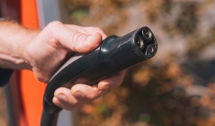 Hand holding an electric vehicle charging plug, symbolizing clean energy and innovation.