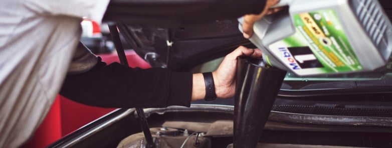 A man in grey overalls filling his car with oil