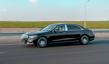 Side on view of a black saloon car driving on the motorway with green fields and a blue sky in the background