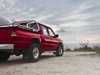 A red pickup truck parked by the rocky coastline under a cloudy sky in Mgarr, Malta.