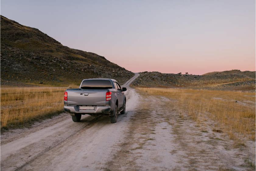 Grey pickup truck driving on a dirt track with mountain in background