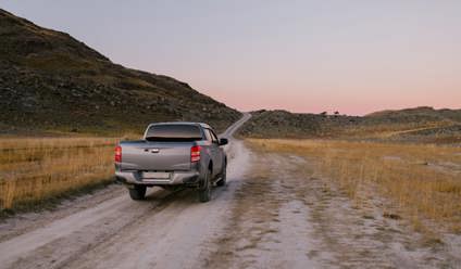 Grey pickup truck driving on a dirt track with mountain in background