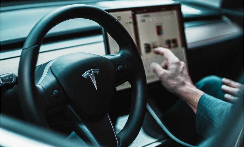 Person sitting behind steering wheel of Tesla car touching the touchscreen