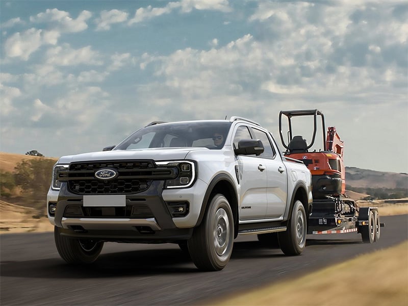 Ford Ranger Plug-in Hybrid pickup truck towing a trailer with an excavator on a rural road