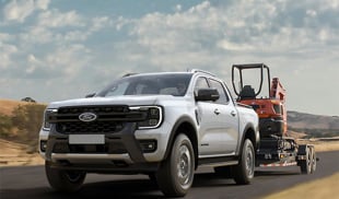 Ford Ranger Plug-in Hybrid pickup truck towing a trailer with an excavator on a rural road