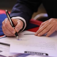 a person signs a document with a pen