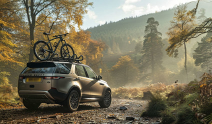 Land Rover Discovery SUV with a mountain bike on the roof parked on a forest trail in autumn