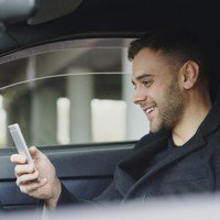 man smiling while looking at his phone in car