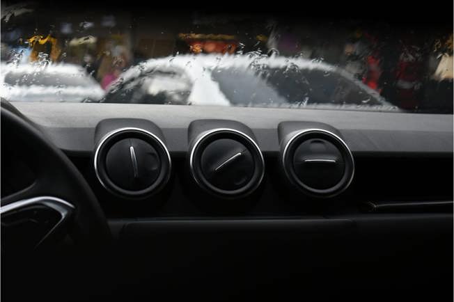 Three air vents sitting on top of a car dashboard with a rainy windscreen in the background