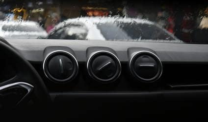 Three air vents sitting on top of a car dashboard with a rainy windscreen in the background