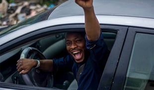 young driver in the car looking happy with his arm raised out of the window in joy