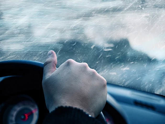 person driving a car with hand on the wheel and wintery conditions outside