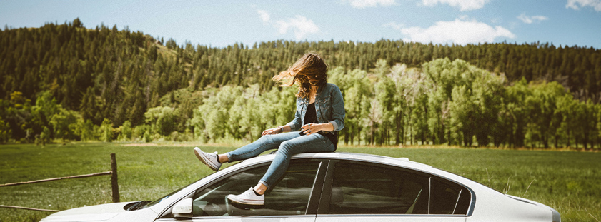 Young woman in denim sitting on car roof