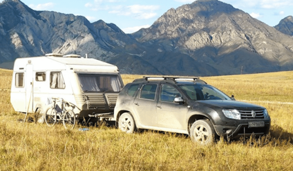 black suv towing a caravan on a grass field in front of mountain range