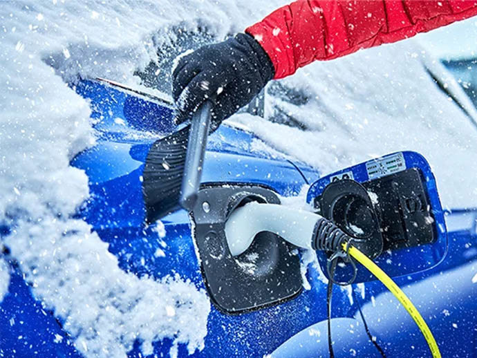 a person’s hand is brushing snow off an electric car while it’s plugged in and charging