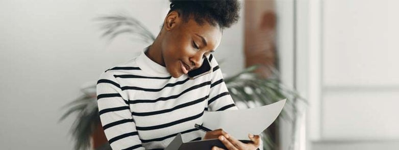 woman multitasking with a phone call and taking notes indoors, wearing stripes