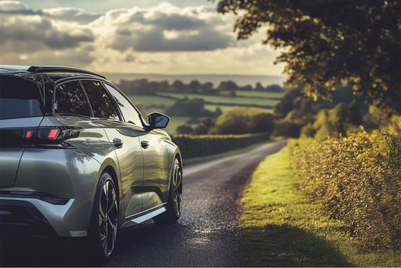 Rear view of a modern estate car on a winding countryside road with rolling green hills