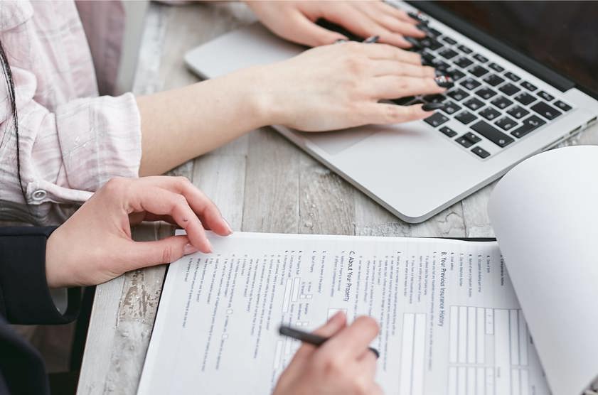 A Person Typing on Laptop Looking at Car Insurance Documents