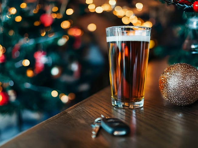 Pint of beer and car keys placed on a table with a festive Christmas background