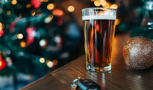 Pint of beer and car keys placed on a table with a festive Christmas background