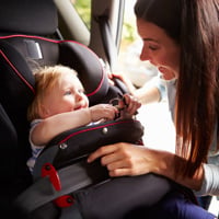 Mother securing infant daughter in car seat