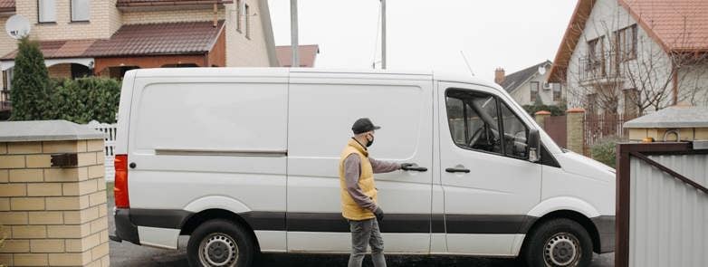 A delivery man exits his van in a suburban residential neighbourhood for home delivery