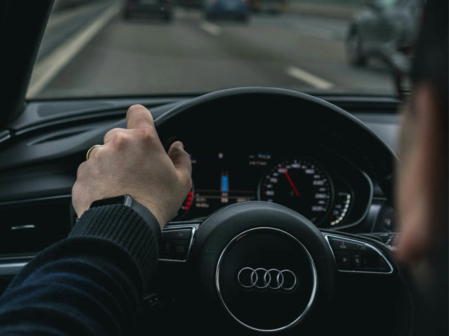 Person driving an Audi car on the motorway with one hand on the wheel