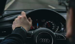 Person driving an Audi car on the motorway with one hand on the wheel