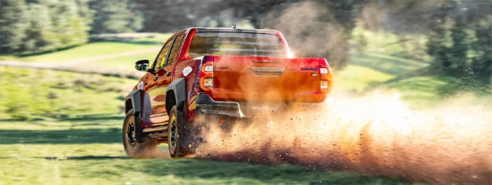 Toyota Hilux GR Sport pickup kicking up dirt while off-roading on a grassy terrain