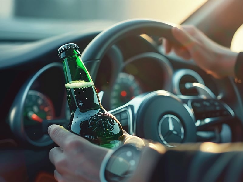 Driver holding a green beer bottle inside a car