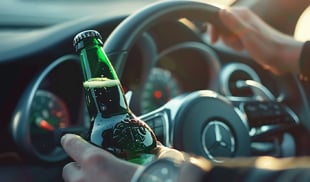 Driver holding a green beer bottle inside a car