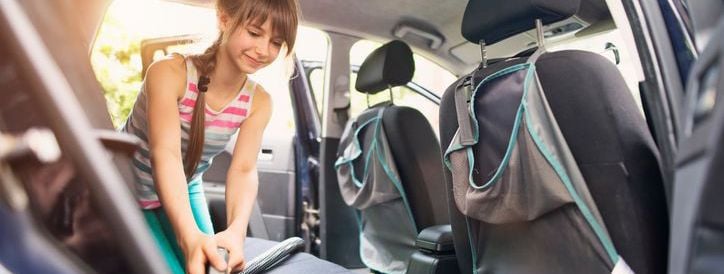 young woman vacuuming the back of a car