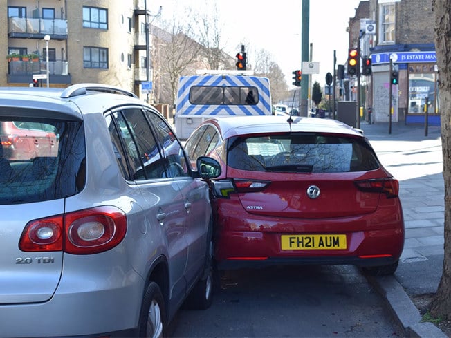 Red Vauxhall and silver Volkswagen involved in a minor parking collision on a busy urban street