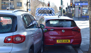 Red Vauxhall and silver Volkswagen involved in a minor parking collision on a busy urban street