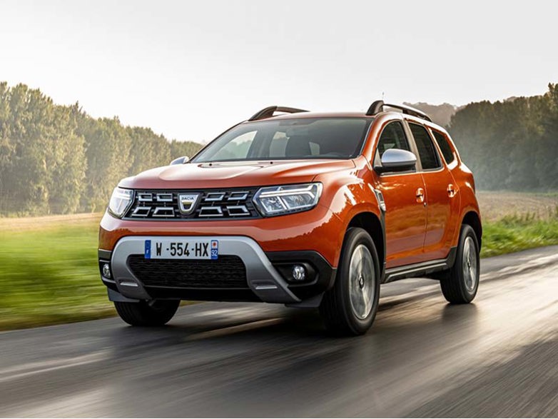 Orange Dacia Duster on a road with woods in the background