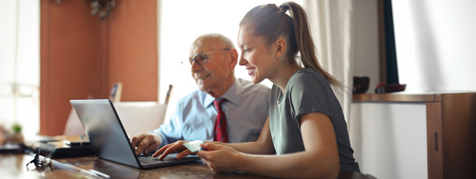 Young woman helping senior man with payment on Internet using laptop