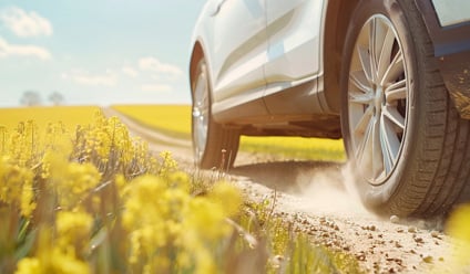 Close-up of a white SUV driving along a dusty country track through a yellow rapeseed field on a sunny spring day in the UK