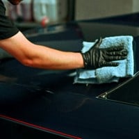 a person polishing a dark blue car with a cloth