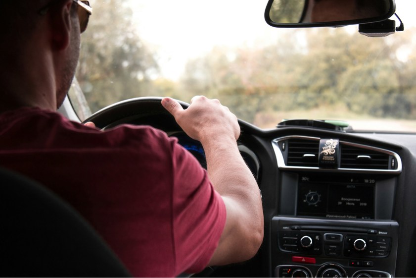 Man in red top driving car with hand on the steering wheel