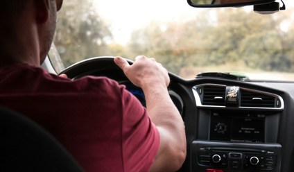 Man in red top driving car with hand on the steering wheel