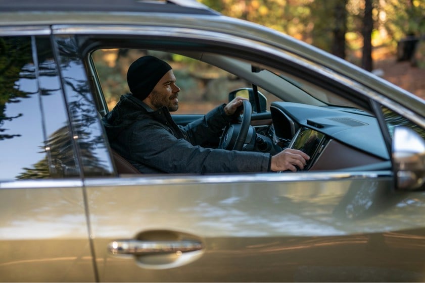 Man with a hat on driving an SUV in the woods