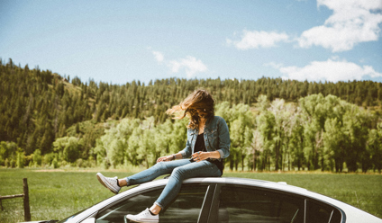 Young woman in denim sitting on car roof